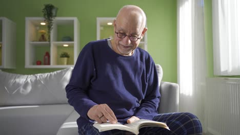 Anciano-Sentado-En-El-Sofá-De-Casa-Junto-A-La-Ventana,-Leyendo-Un-Libro.